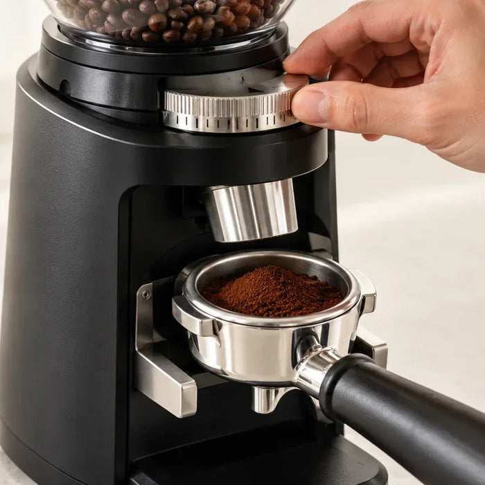 Adjusting an espresso grinder with fine coffee grounds in a portafilter.