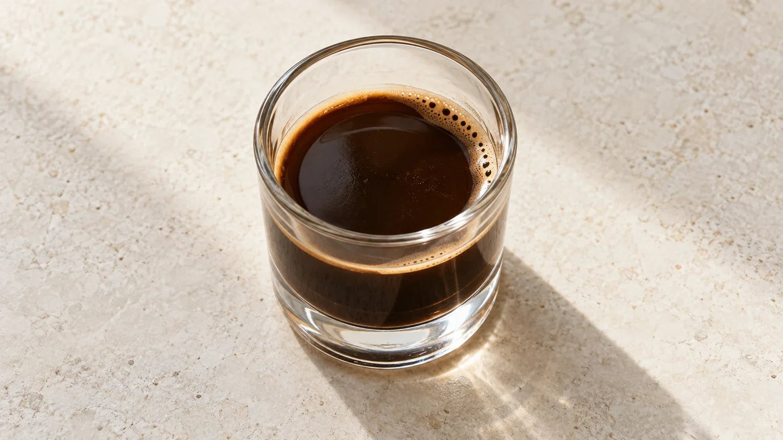 Espresso with a mostly exposed dark surface and a thin trace of crema in a short glass.