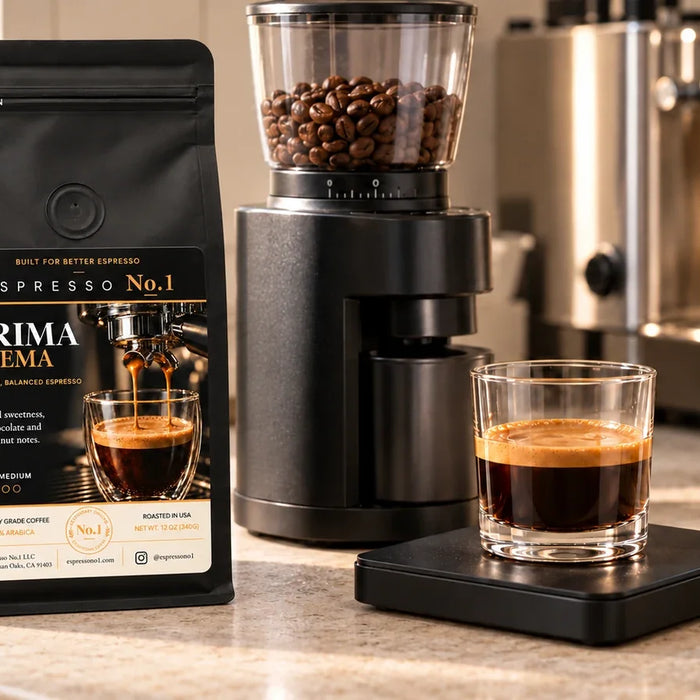 A Prima Crema coffee bag beside a burr grinder and espresso in a short clear glass on a black scale.