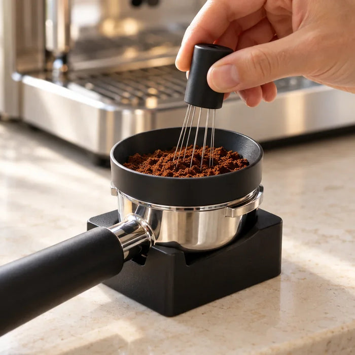 A hand using a fine-needle WDT tool in a portafilter fitted with a dosing funnel.